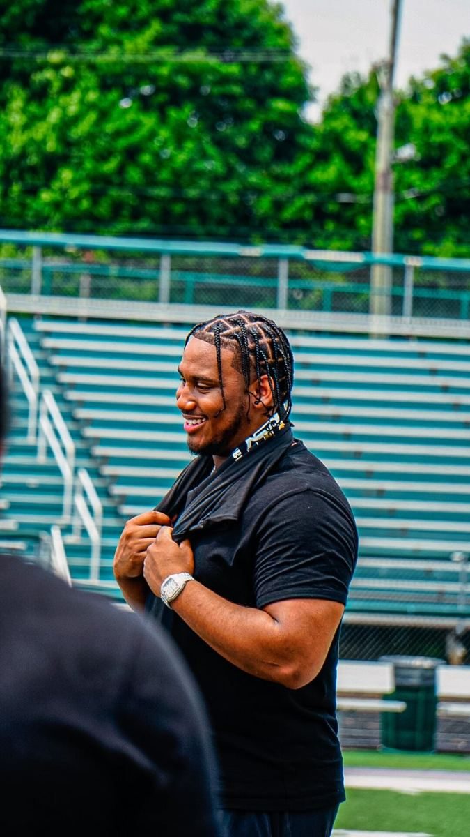 A coach smiling on the sidelines of a football field